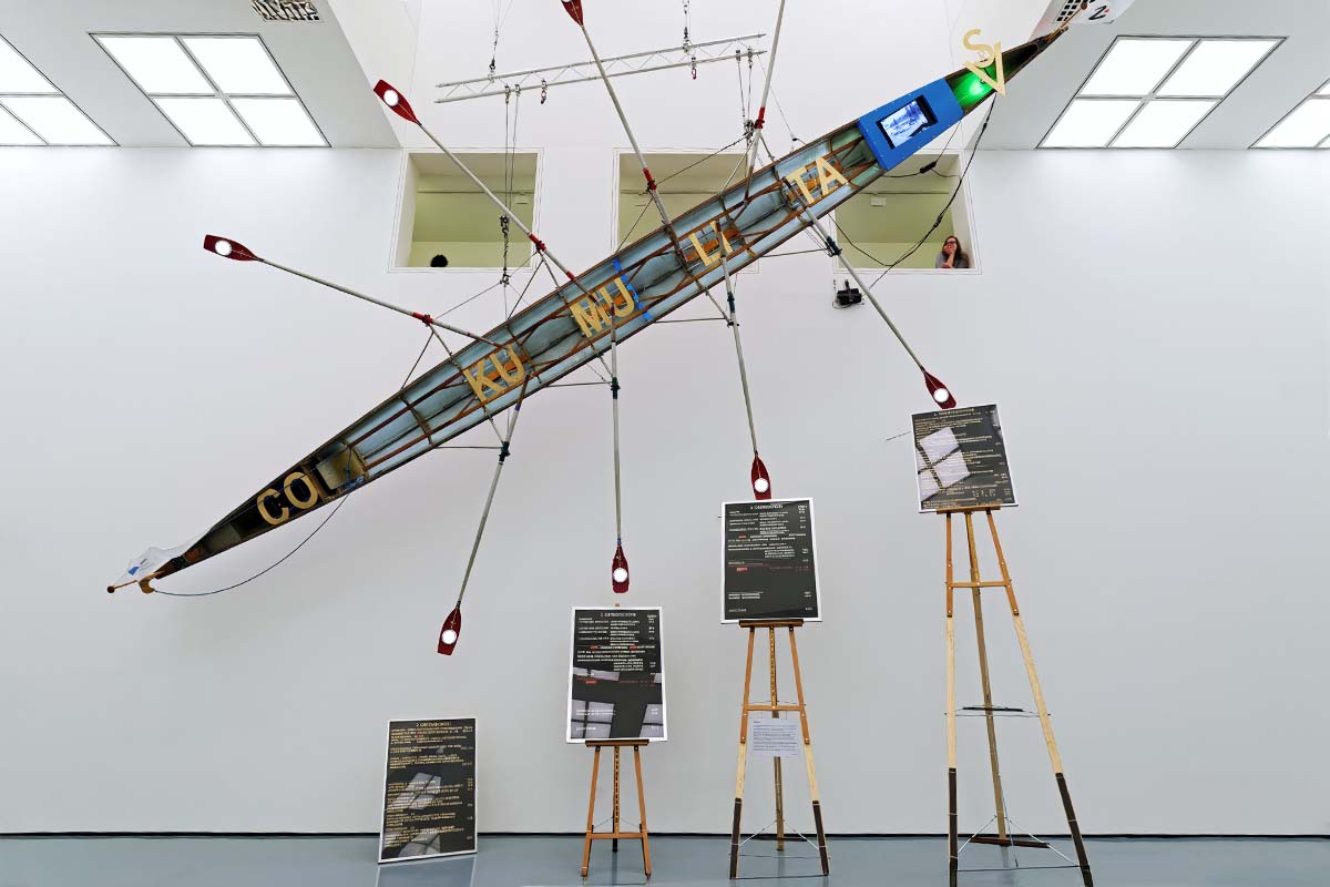 Schräg aufgehängtes Ruderboot mit Rudern in Kunstausstellung, Tafeln auf Staffeleien.